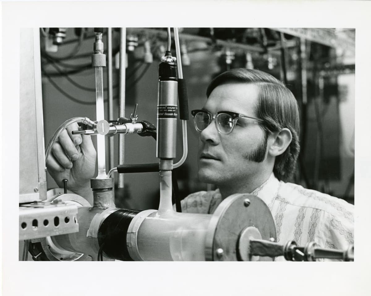 Investigador trabajando con un espectrómetro de microondas y tubos de gas en un laboratorio.