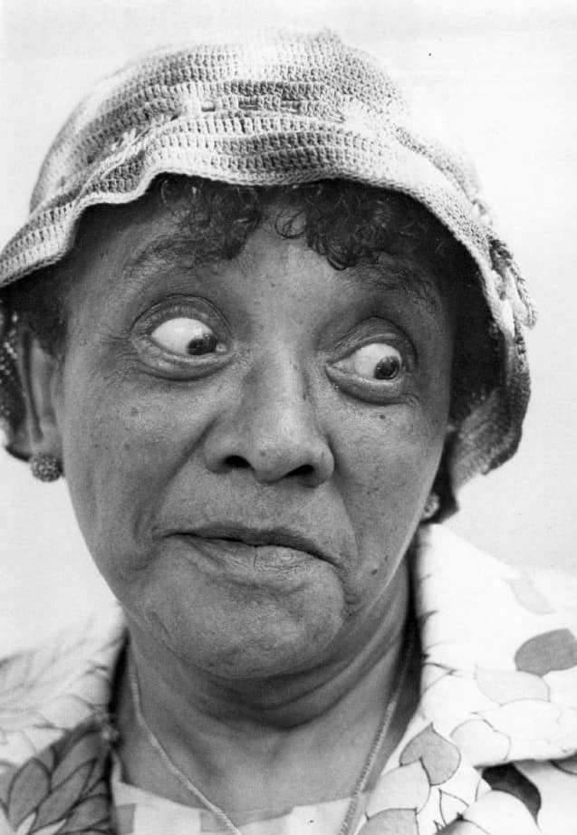Primer plano en blanco y negro de Moms Mabley con sombrero tejido, mirando de lado con expresión cómica durante una aparición televisiva de 1968.