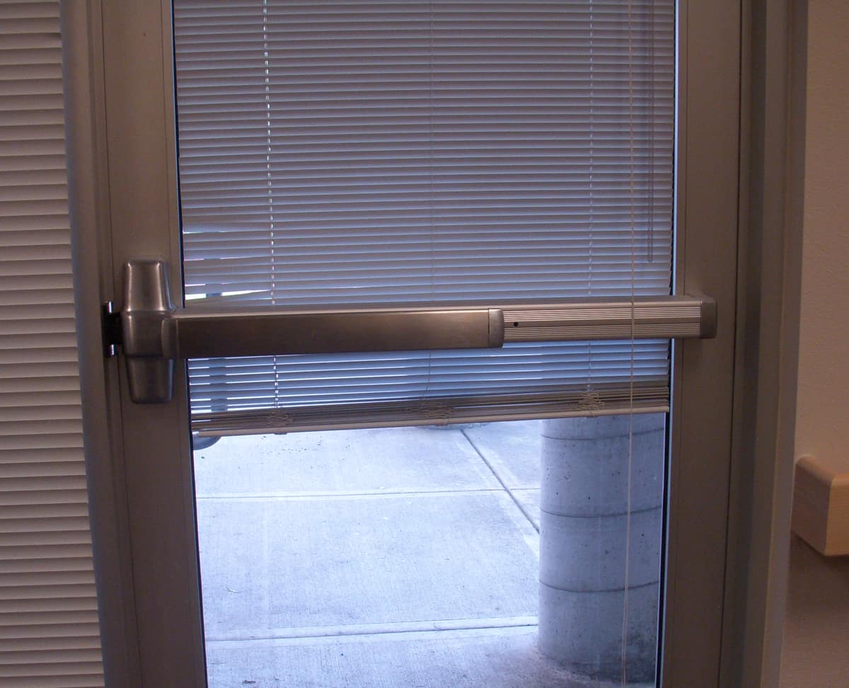 Puerta de cristal equipada con una barra horizontal antipánico para abrirla empujando.