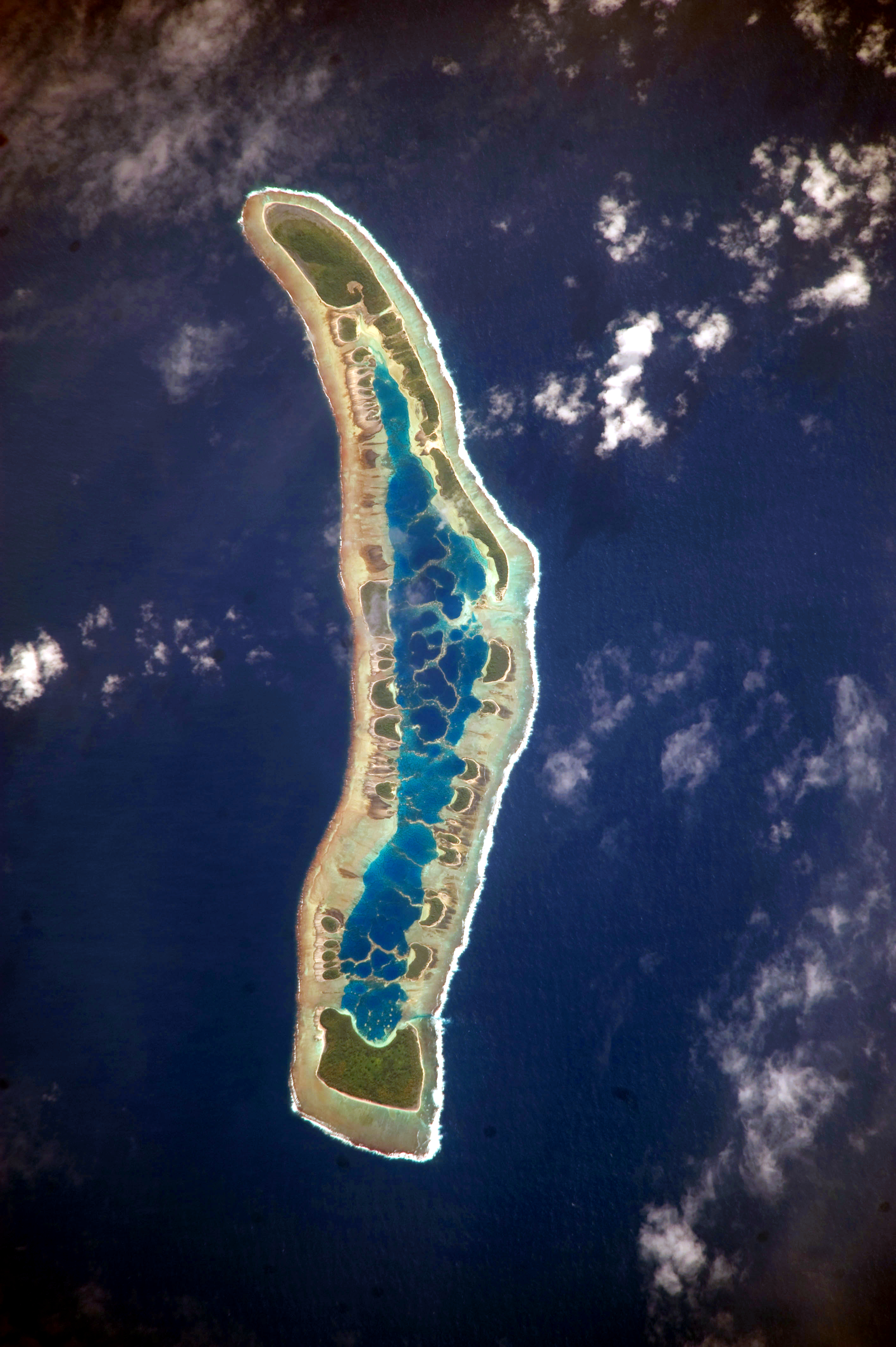Vista orbital de un atolón estrecho de Kiribati, con isletas verdes alrededor de una laguna turquesa en medio del océano Pacífico.