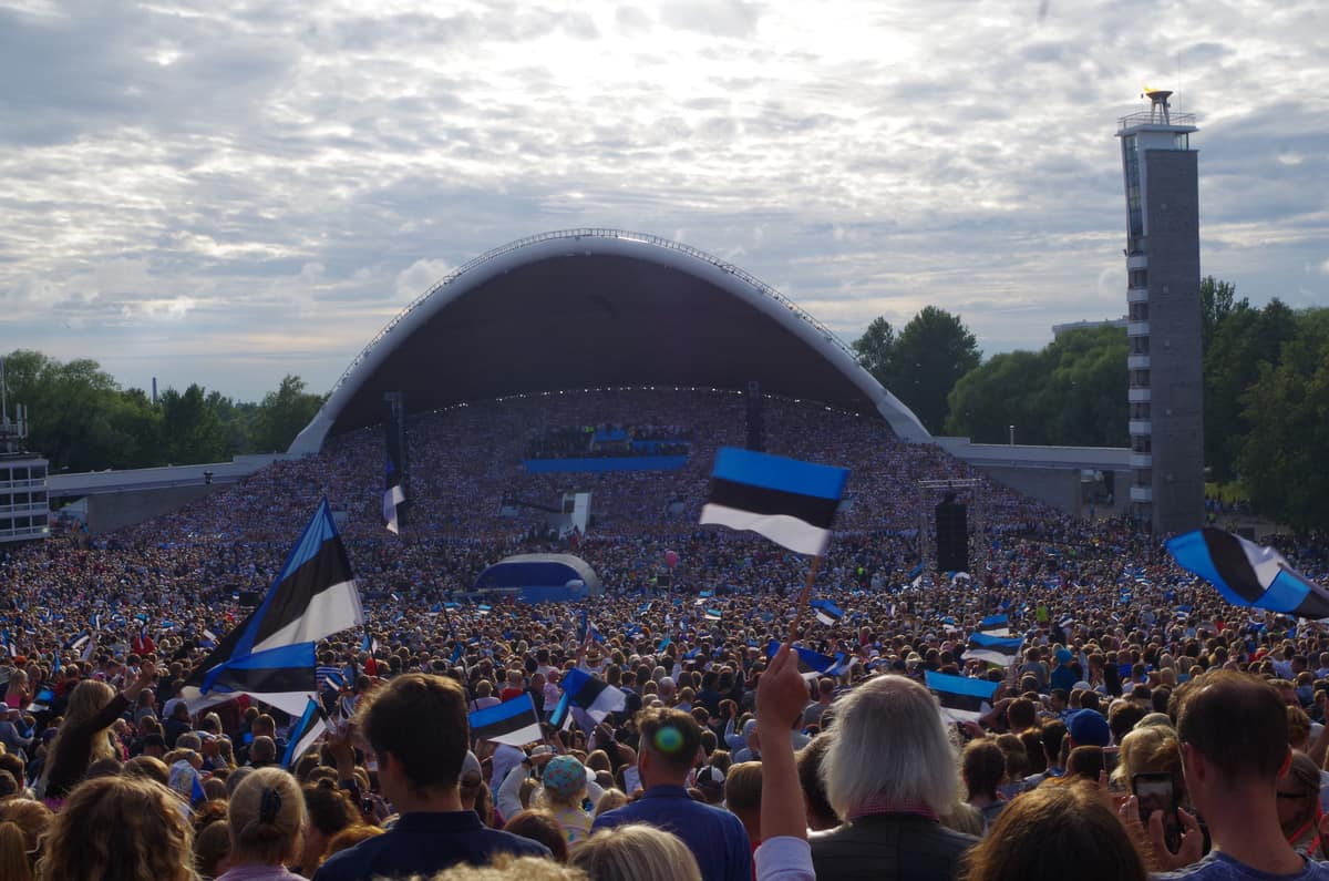 Una multitud llena el recinto del Festival de la Canción de Tallin y ondea banderas de Estonia frente al gran escenario coral.
