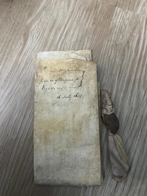 Documento manuscrito antiguo de pergamino con líneas de texto y un sello de cera oscuro colgando en la parte inferior.