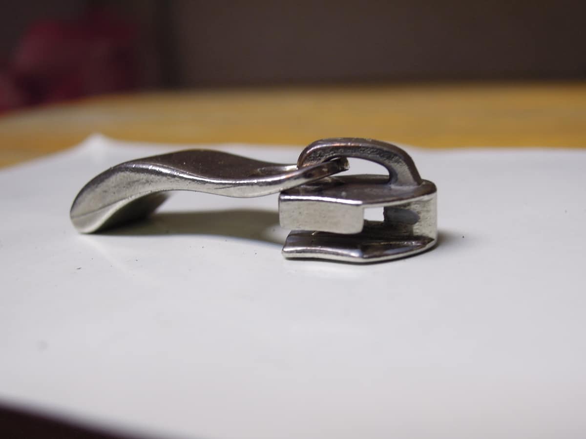 Primer plano de un cursor metálico de cremallera y la abertura por la que pasan las dos filas de dientes.