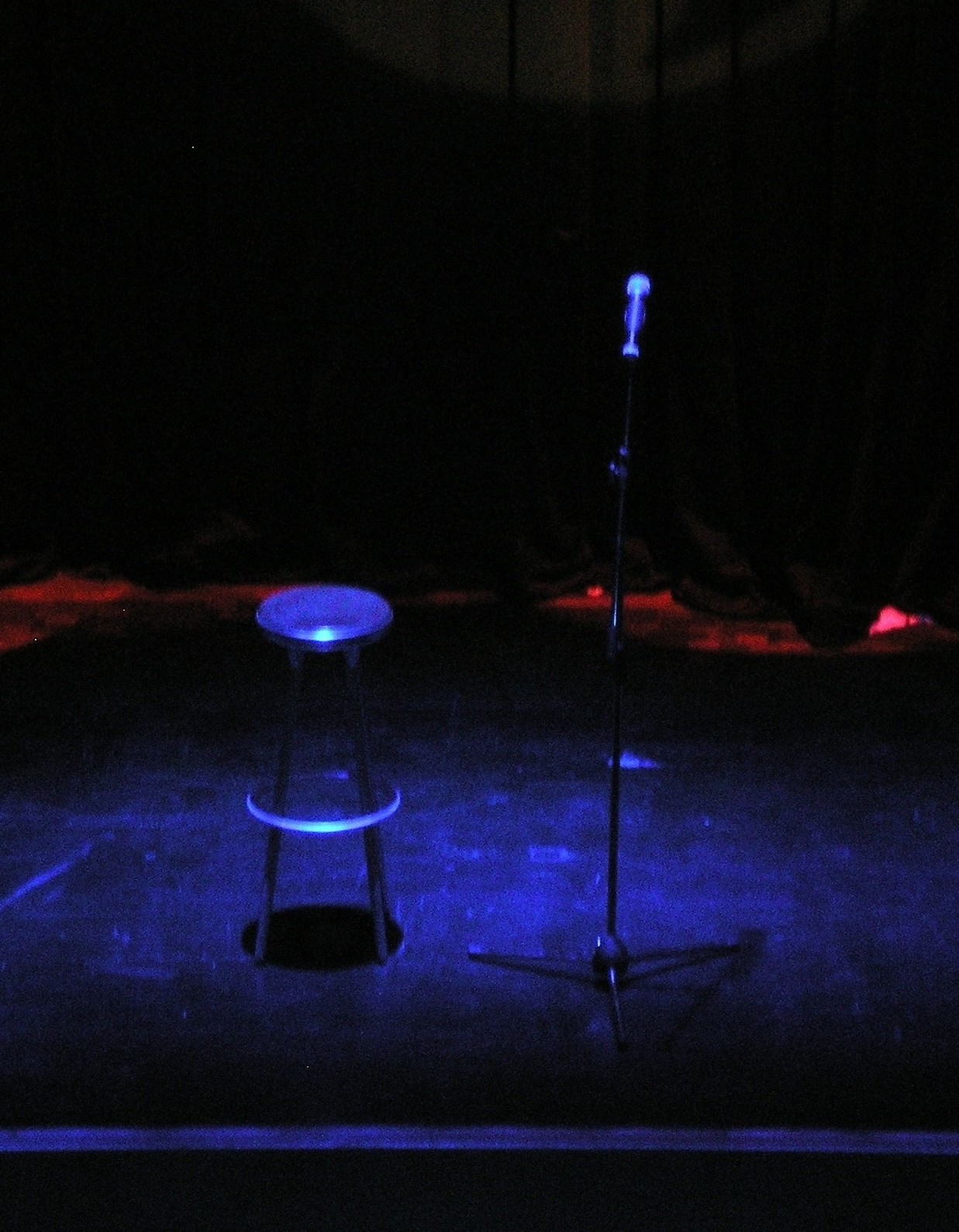 Escenario vacío de comedia en vivo con micrófono y cortina roja.