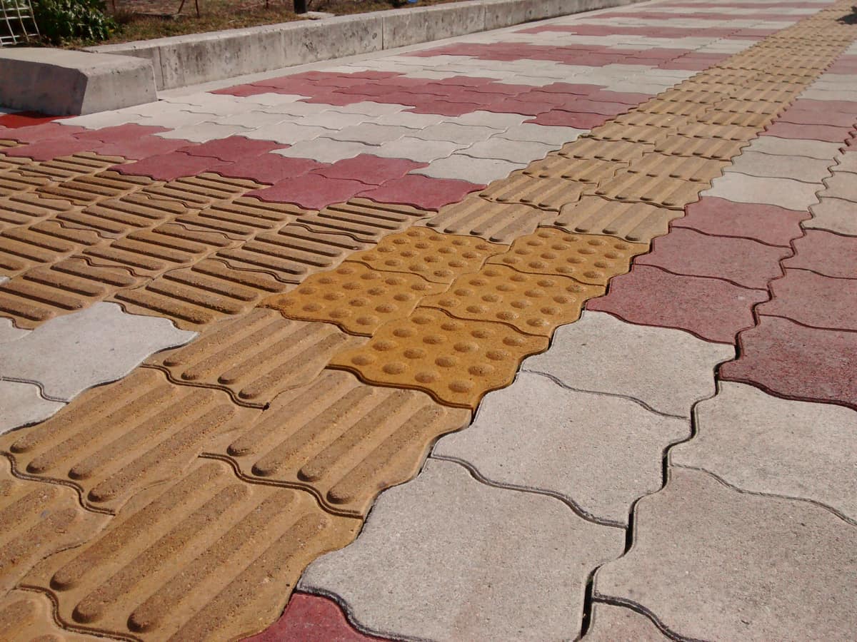Baldosas táctiles amarillas con líneas longitudinales que convergen en una zona de puntos sobre una acera japonesa.