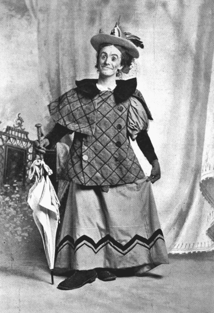 Dan Leno posa de cuerpo entero con vestido, sombrero y paraguas como la Baroness de Cinderella en 1896.