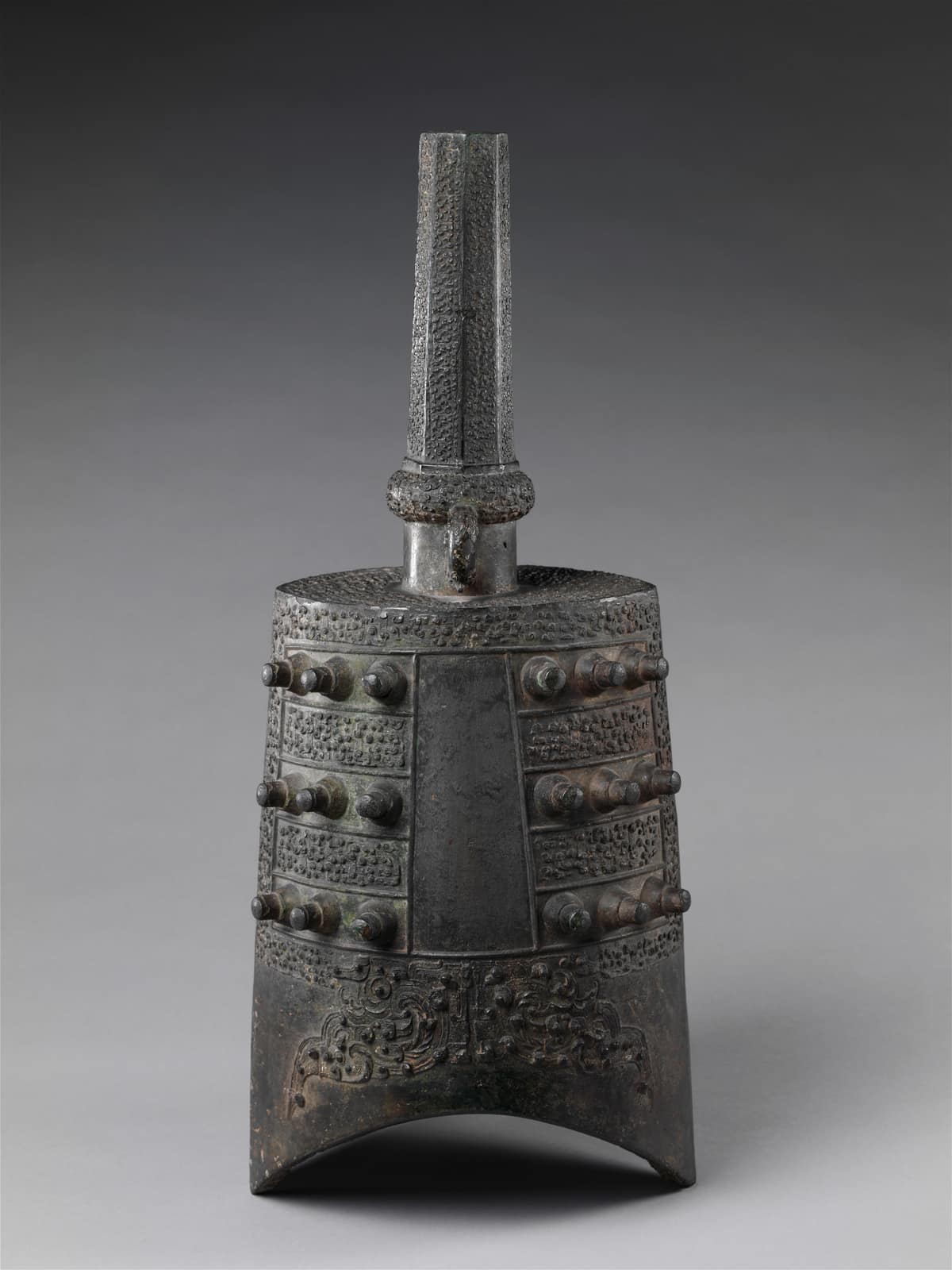 Campana ritual china de bronce, alta y estrecha, con filas de salientes y decoración geométrica, fechada entre los siglos V y III antes de nuestra era.