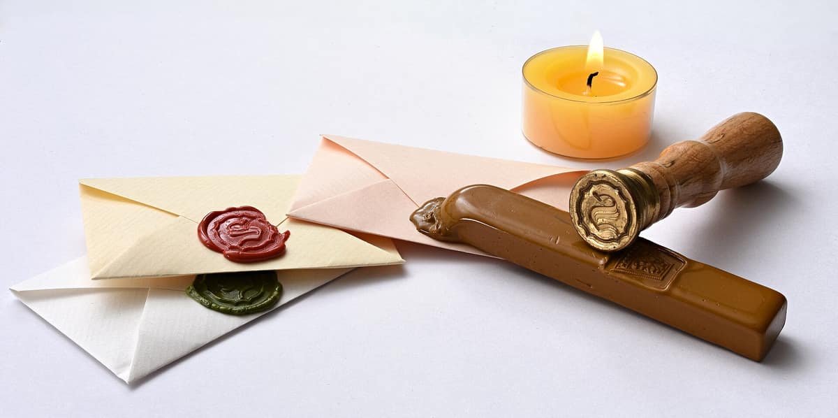 Varias cartas de papel cerradas con sellos circulares de cera roja junto a una barra de lacre.